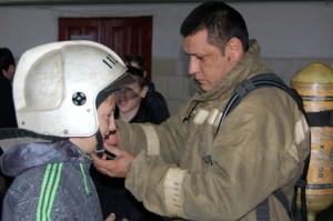 Пожарный С. Б. Олимов помогает семикласснику надеть защитный шлем
